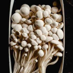Photo by Eva Bronzini A close-up of fresh enoki mushrooms arranged in a packaging box, highlighting their unique texture.